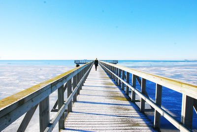 Back of woman waling on pier against clear blue sky