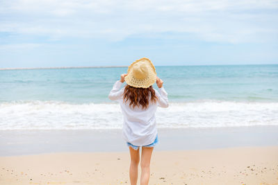 Rear view of woman standing at beach against sky