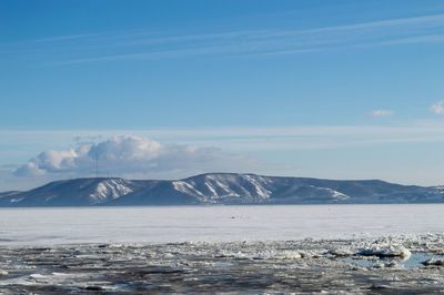 Scenic view of sea by snowcapped mountains against sky