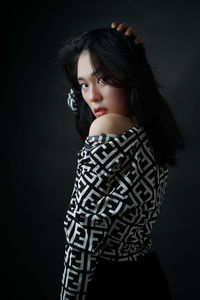 Young woman looking away while standing against black background