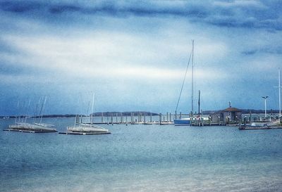 Sailboats in sea against cloudy sky