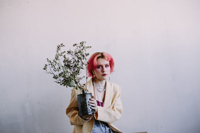 Young woman with potted plant standing against wall
