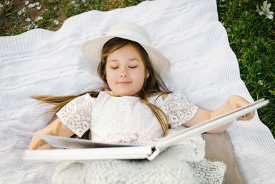 A little beautiful girl lies on a blanket in the garden and looks at a family or parent wedding