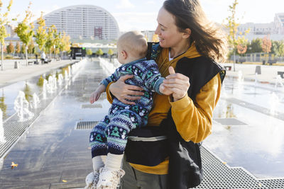 Mother playing with son at urban park by fountains