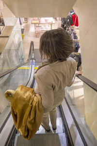 Rear view of mature woman moving down on escalator