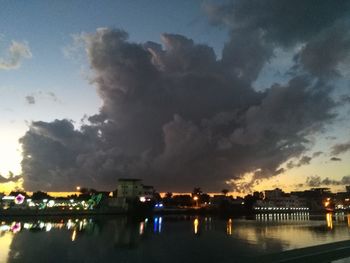 River by illuminated city against sky at sunset