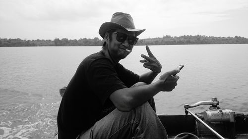 Side view of man showing peace sign in boat on lake