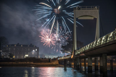 Low angle view of firework display over river against sky at night