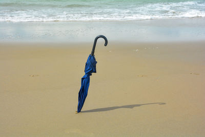 A closed umbrella is stuck in the sand, on the beach in the sunlight