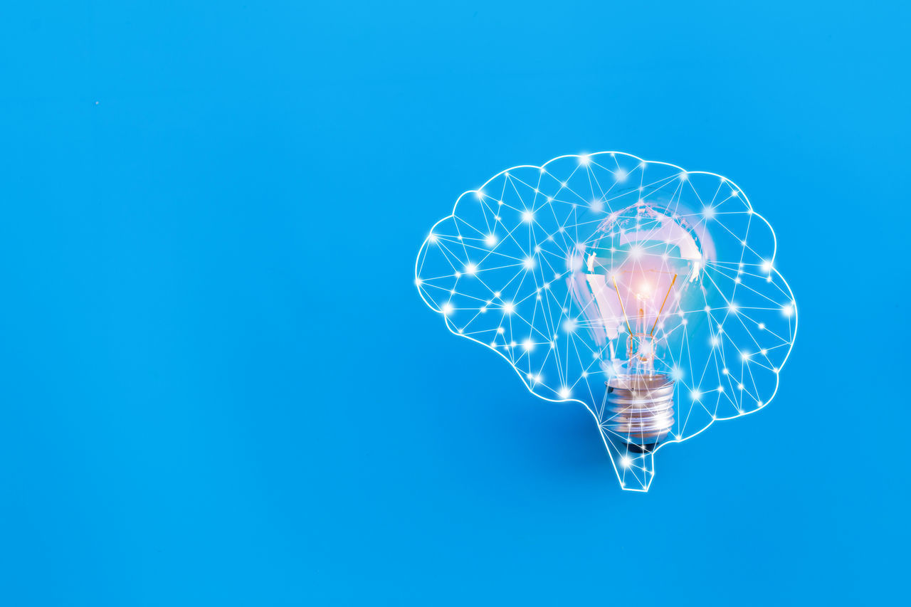 ILLUMINATED LIGHT BULB AGAINST BLUE SKY