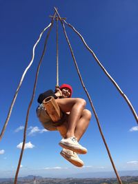 Low angle view of woman enjoying on rope swing against blue sky