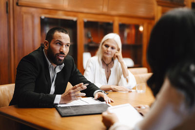 Male financial advisor discussing over contract document with female colleagues in board room