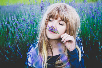 Beautiful young woman smelling lavender flowers while sitting in lavender field