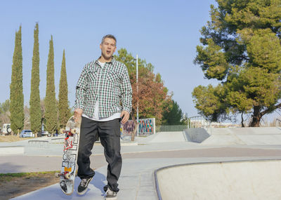Portrait of man with skateboard walking in park