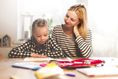 Girl studying while sitting with mother at home