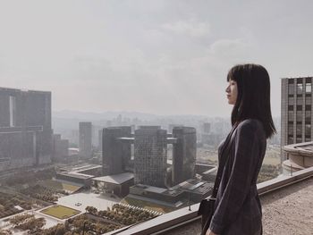 Side view of woman standing by cityscape against sky