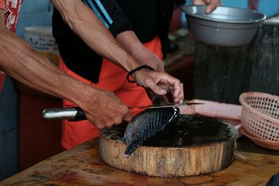 Cropped hand of man cutting fish on board
