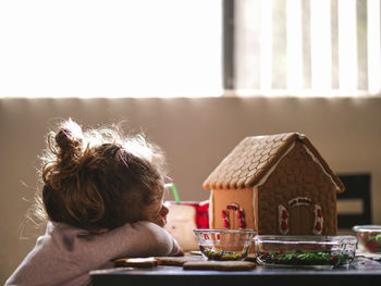 Girl resting by gingerbread house on table at home