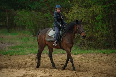 Teenage girl looking away while sitting on horse on field against trees