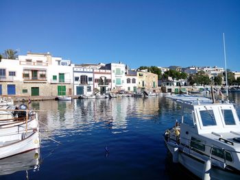 Sailboats moored on canal by buildings against clear blue sky