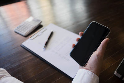 Cropped hand of businessman using mobile phone on desk in office