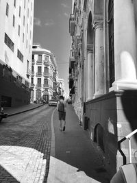 Rear view of man walking on street amidst buildings