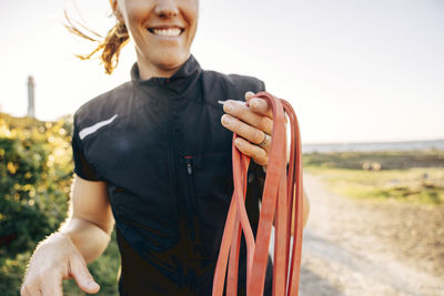 Midsection of smiling female coach holding resistance band at beach