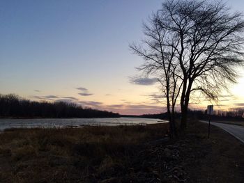 Bare trees on field against sky during sunset