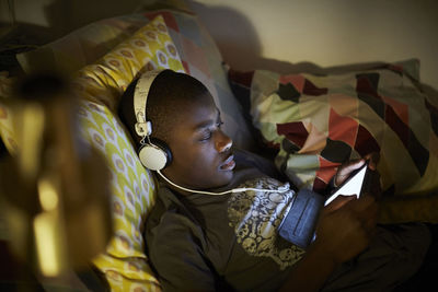 High angle view of boy wearing headphones and using digital tablet while lying on bed