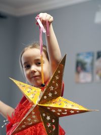 A little girl in a festive red dress is busy decorating the room with a paper gold star. new year 
