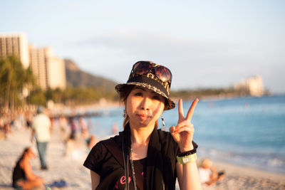 Portrait of young woman standing at beach against sky