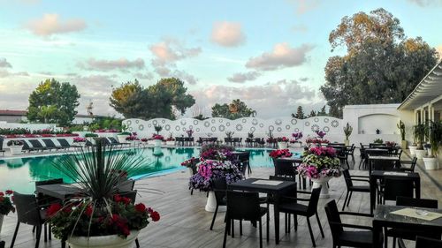 Empty chairs and tables by swimming pool against sky