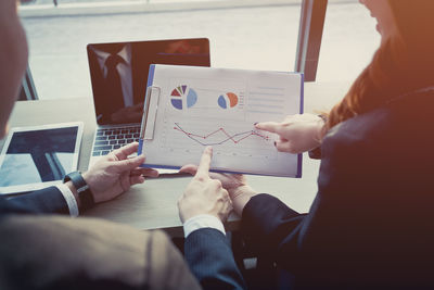 Midsection of colleagues discussing over chart at office