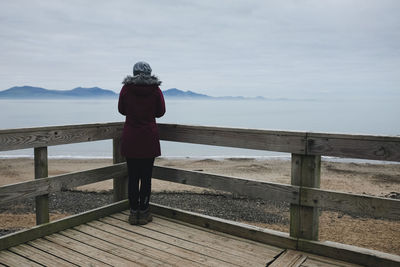 Rear view of woman standing on railing against sea