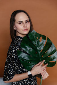 Woman in a black dress with polka dots on a brown background holding a petal of a tropical plant