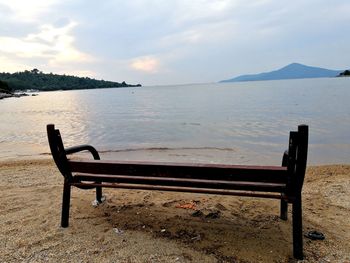 Empty bench by sea against sky