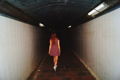 Rear view of woman walking in illuminated tunnel