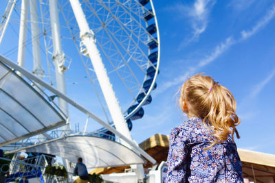 Rear view of woman with ferris wheel against blue sky