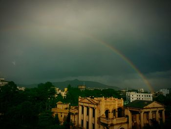 Rainbow over city against cloudy sky