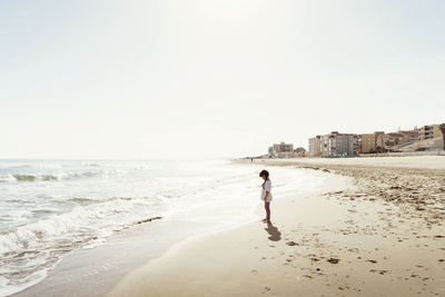 Rear view of girl walking at beach against clear sky