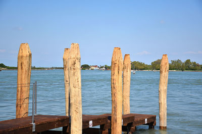 Wooden posts in sea against blue sky