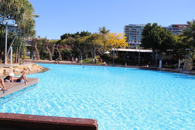 Swimming pool by trees against clear blue sky