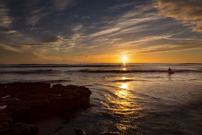 Silhouette person in sea against sky during sunset