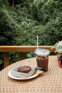 Close up of a plastic of iced cocoa cool drink and chocolate cake on table.