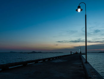 Illuminated lamp on pier over sea at sunset