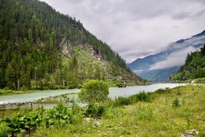 Scenic view of lake in forest and mountains against  cloudy sky