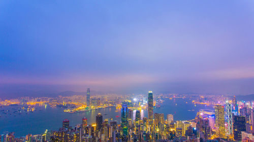 River in illuminated city against sky during sunset