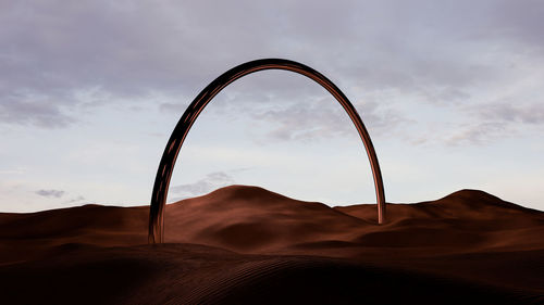 Desert dune landscape at sunset with a metal bow shaped monolith