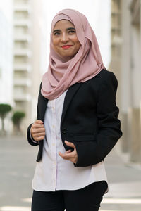 Smiling businesswoman wearing hijab while standing against building