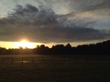 Scenic view of landscape against cloudy sky at sunset